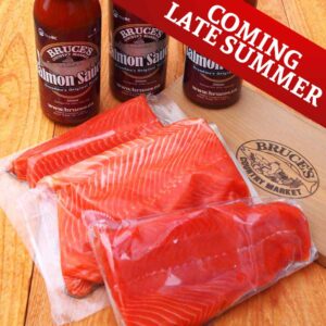 Packaged salmon on a wooden countertop with salmon sauce in bottles in background.