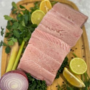 White Spring Salmon on a cutting board with lemons, herbs and an onion.